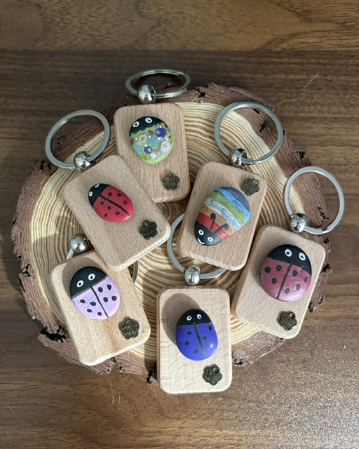 Hand-painted pebble bug and ladybird key rings displayed on a wooden slice